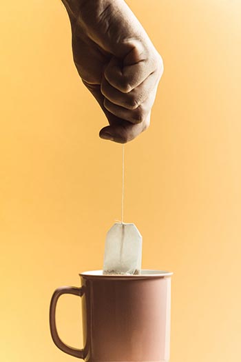 Hand holding a tea bag over a cup.