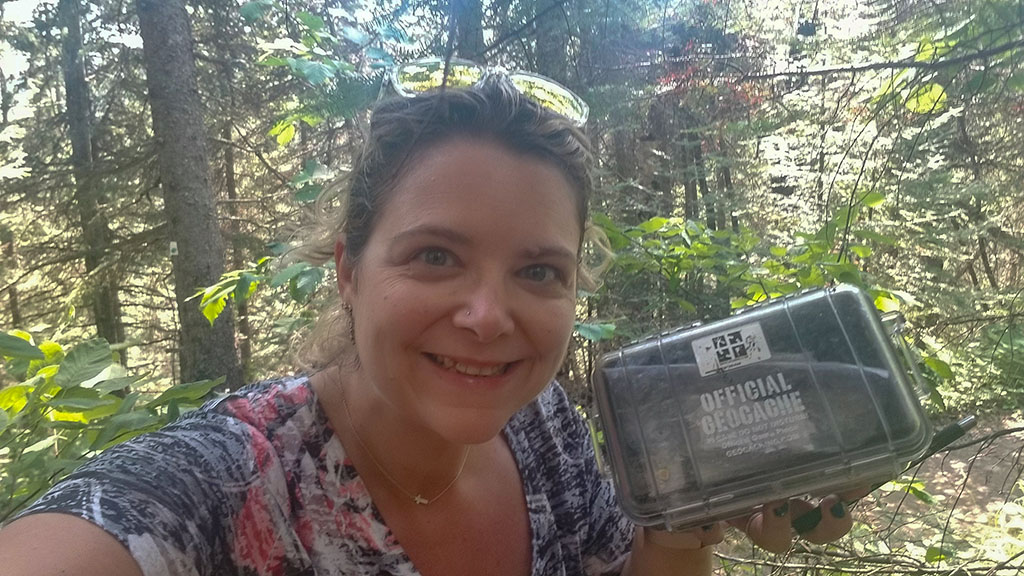 Michelle holding up an Official Geocache in the woods